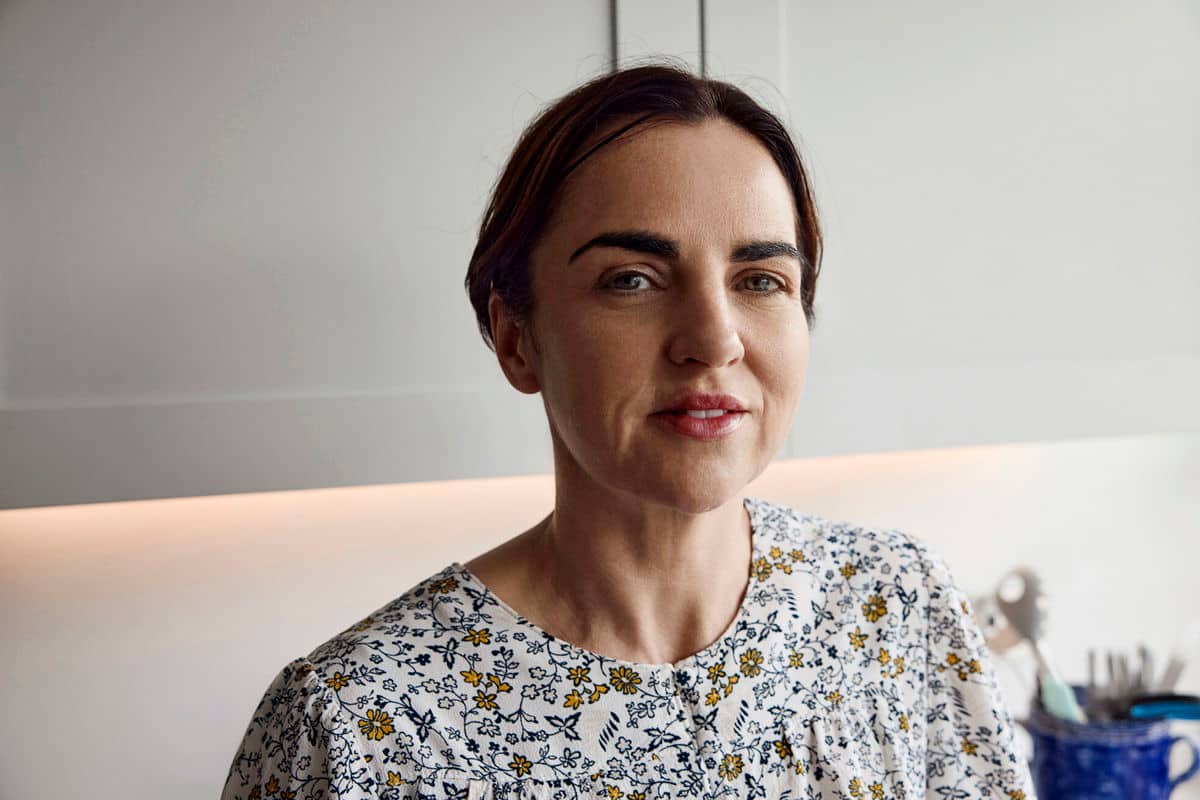 Frau mit Blumen-Oberteil steht in einer weissen Kueche und schaut nach vorne