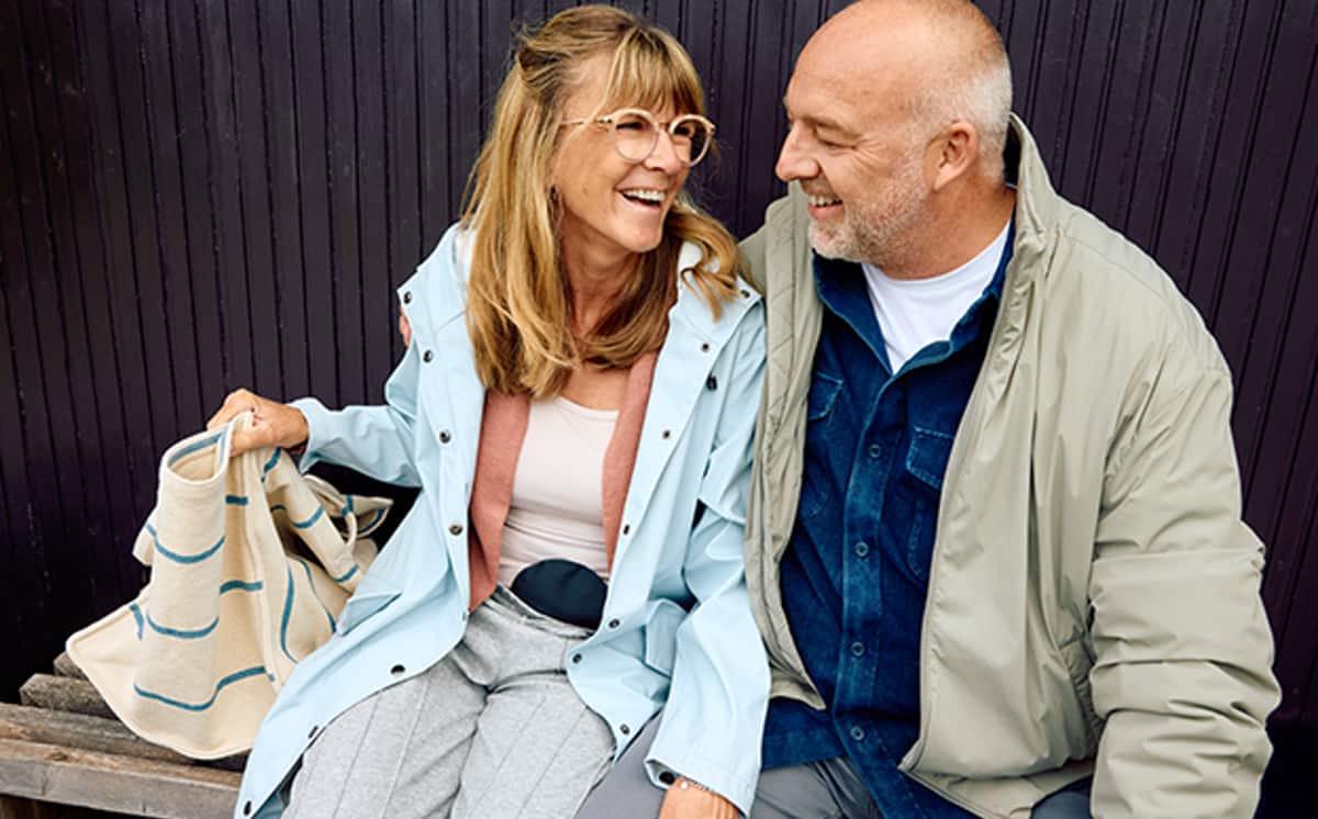 Frau mit schwarzem Stomabeutel am Bauch sitzt neben Mann und lächelt